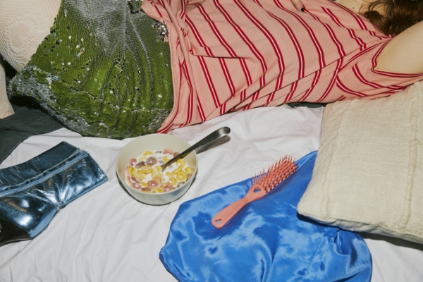 I Took Half A Mythic Blend Gummy And Now My Tv Is Watching Me 2 A High-Angle, Cluttered Shot Of A Person Reclining On A White Bed Sheet. The Individual Is Wearing A Pink And Red Striped T-Shirt And A Green Sequined Skirt. Scattered Around Them On The Bed Are Various Items: A Bowl Of Colorful Loop Cereal With Milk And A Silver Spoon, A Metallic Blue Boot, A Pink Hairbrush Resting On A Piece Of Bright Blue Satin Fabric, And A Textured Off-White Pillow. The Composition Creates A Candid, &Quot;Lived-In&Quot; Aesthetic With A Focus On Contrasting Colors And Textures.